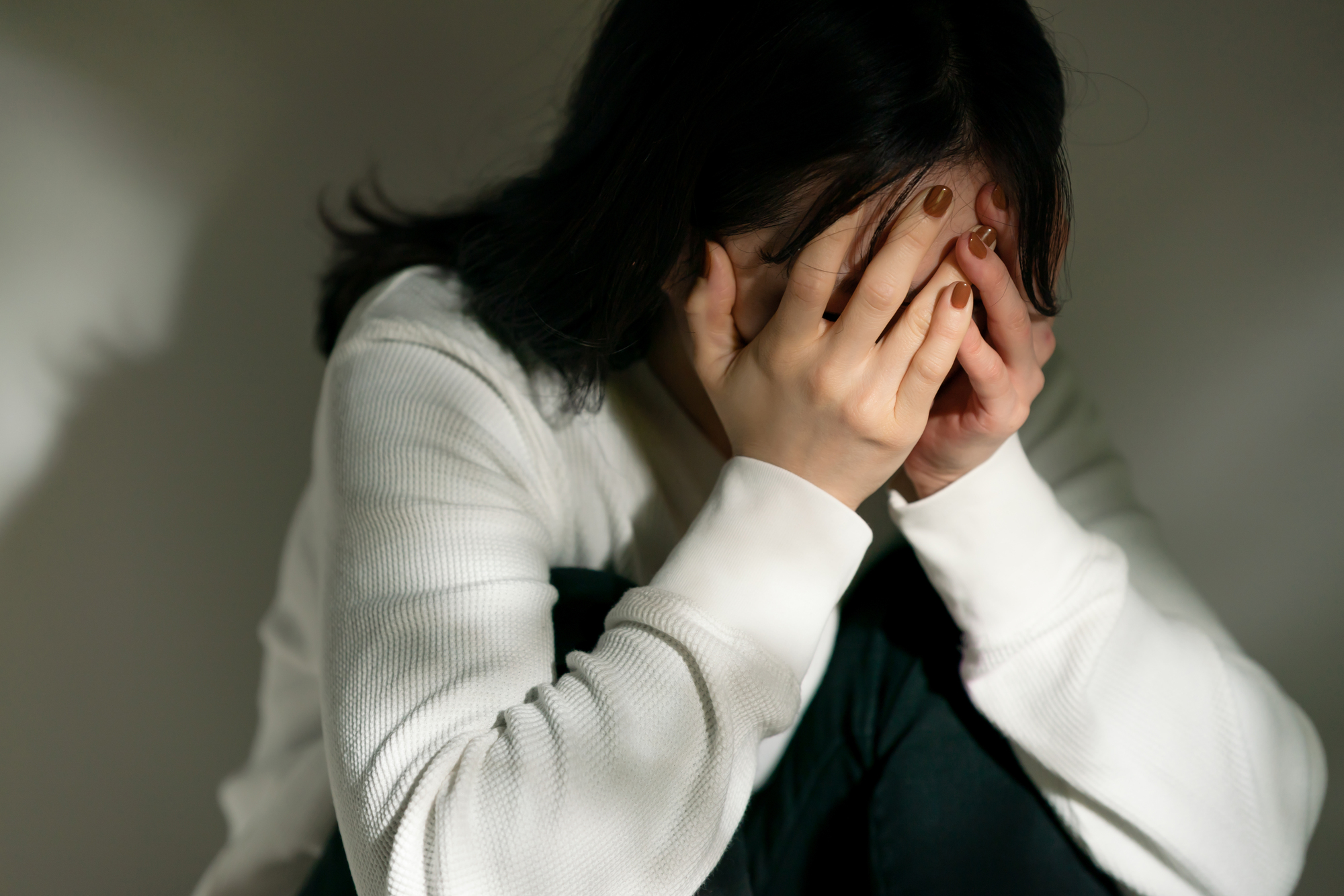 両手で顔を覆ってうつむく女性