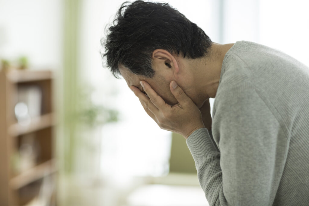 両手で顔を覆って悩む男性