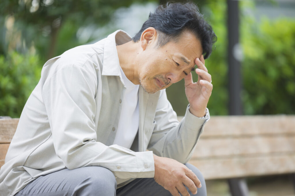 ベンチで頭を抱えて考え込む男性