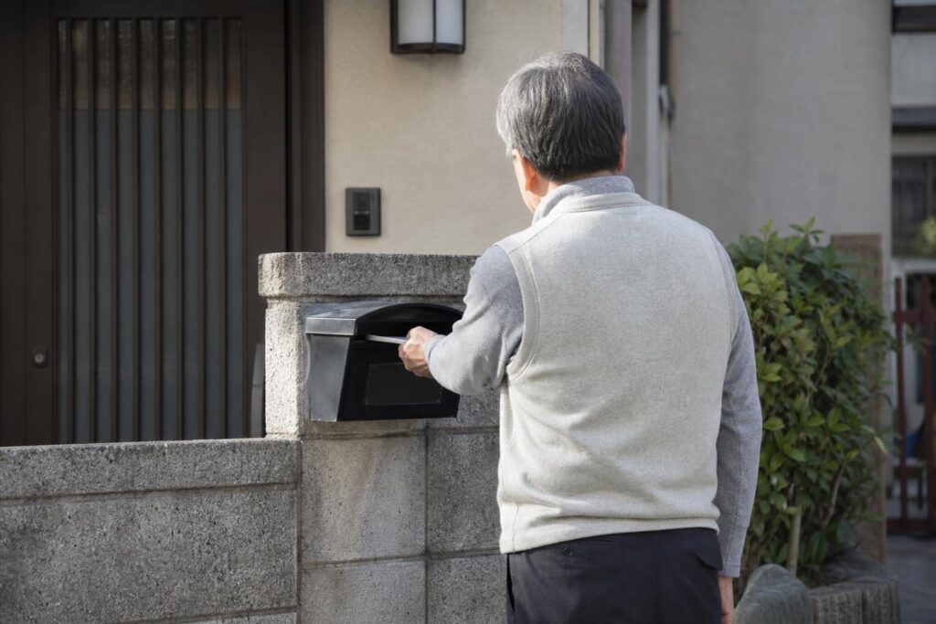 自宅の郵便受けを確認する高齢者の後ろ姿