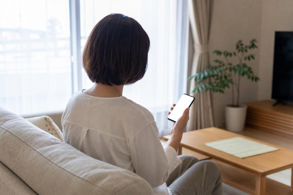 明るい部屋でスマートフォンを見つめる人物の後ろ姿