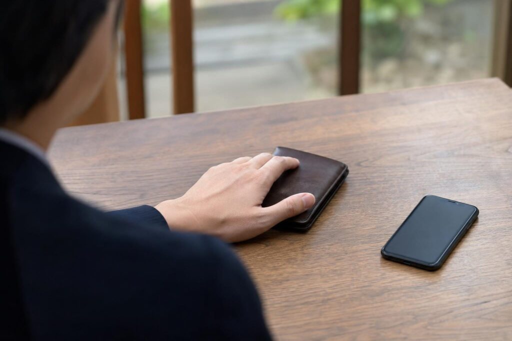 閉じた財布に手を置く手元と伏せたスマホ